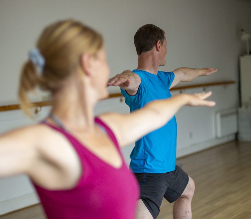 A man and woman in warrior pose, enjoying a yoga class